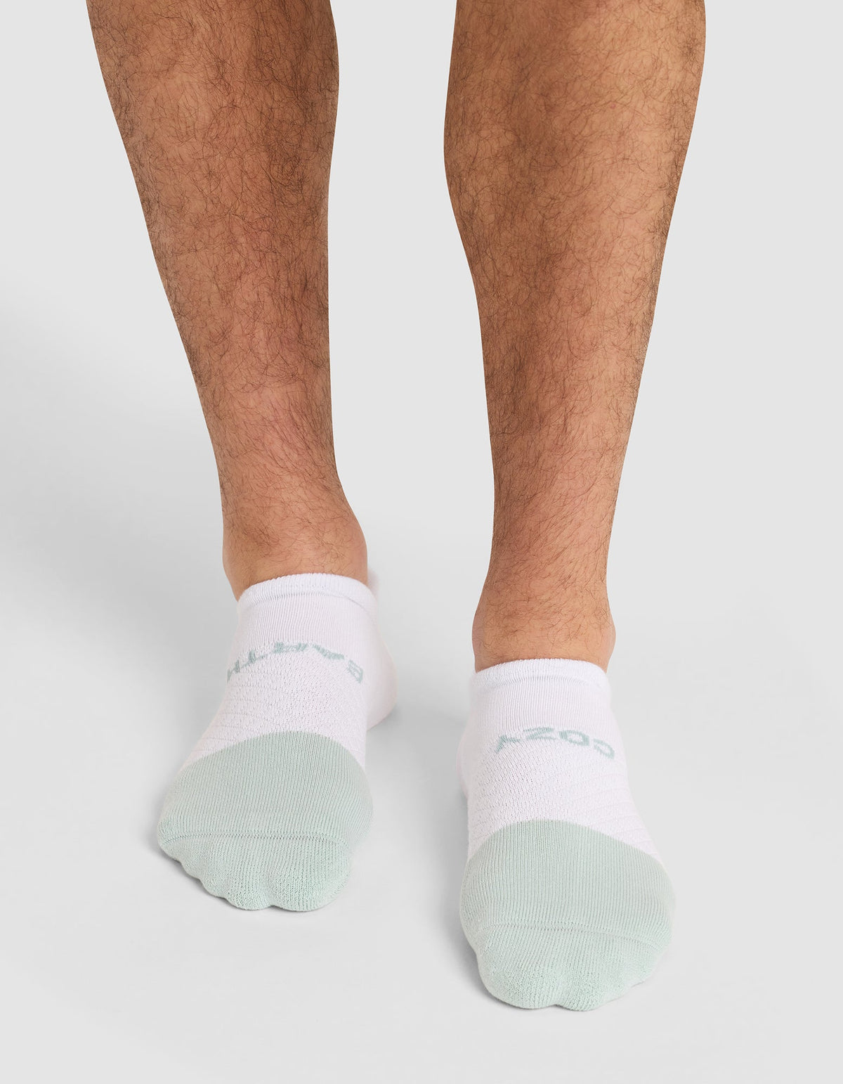 A person wears Cozy Earth Essential Ankle Socks in white and light green, standing on a light background with only their lower legs and feet visible. |Color:Arctic