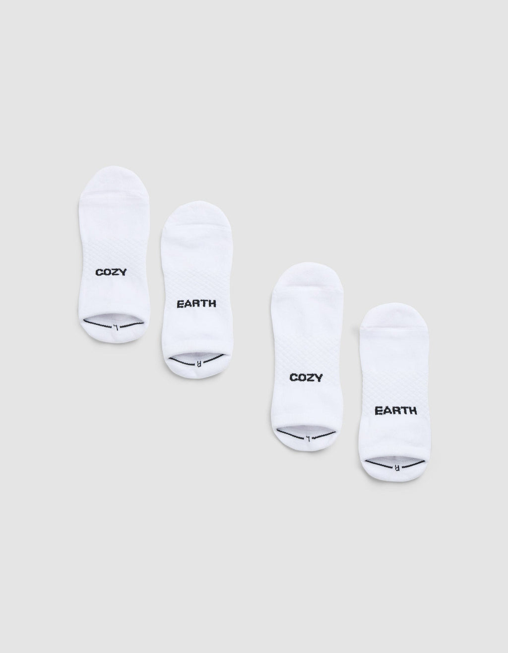 Two pairs of Cozy Earth Essential Ankle Socks are displayed side by side on a light gray background, each featuring black text near the toes—one in each pair reads "COZY" and the other reads "EARTH. |Color:White