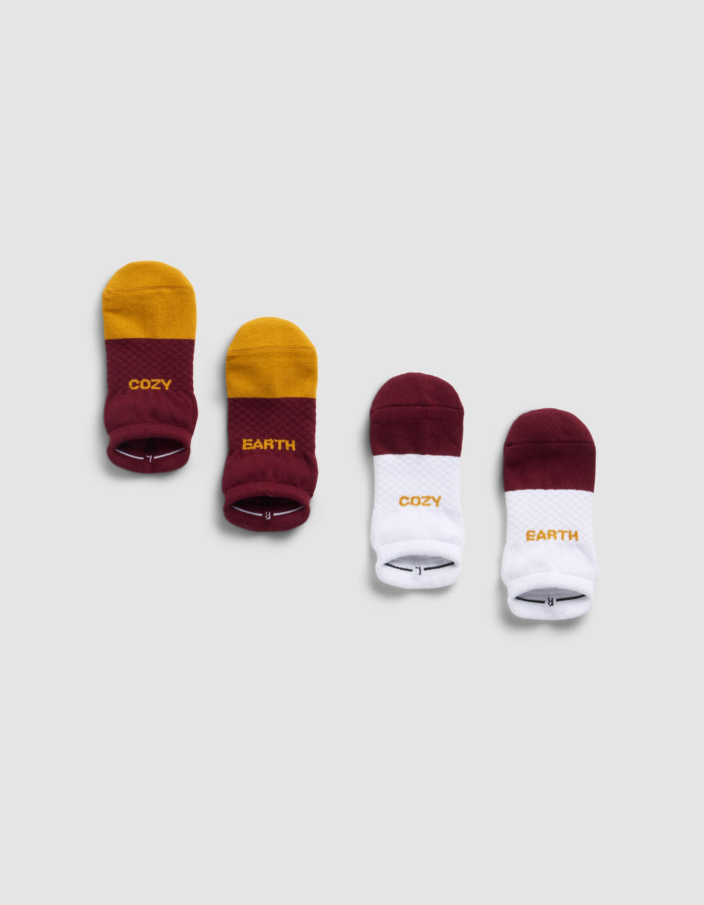Four pairs of Cozy Earth Essential Ankle Socks on a gray background: the left pair is yellow and burgundy with "COZY" and "EARTH" text, the right pair is burgundy and white with the same words on each sock.|Color:Burgundy