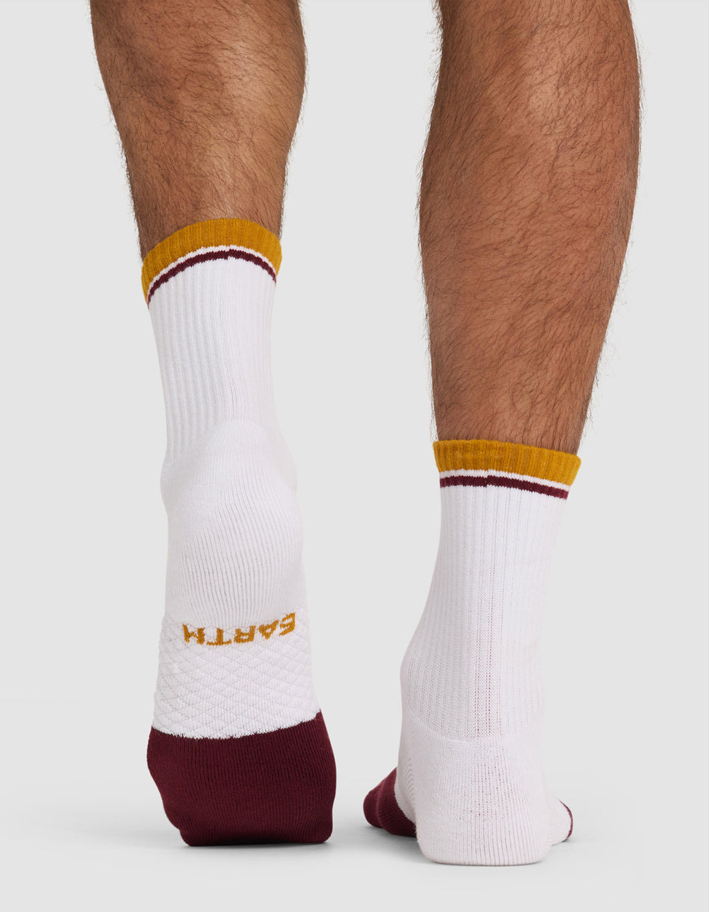 A person wears Cozy Earth Essential Calf Socks—white with gold "EARTH" on the sole, maroon heel and toe, and gold/maroon accents—standing on a white surface.|Color:Burgundy
