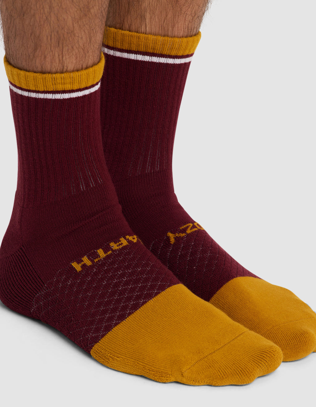 Two feet wear Cozy Earth's Essential Calf Socks in maroon with mustard yellow toes, heels, and cuffs, plus a white stripe near the top. “EARTH” is printed in yellow on one sock, “COZY” on the other.|Color:Burgundy