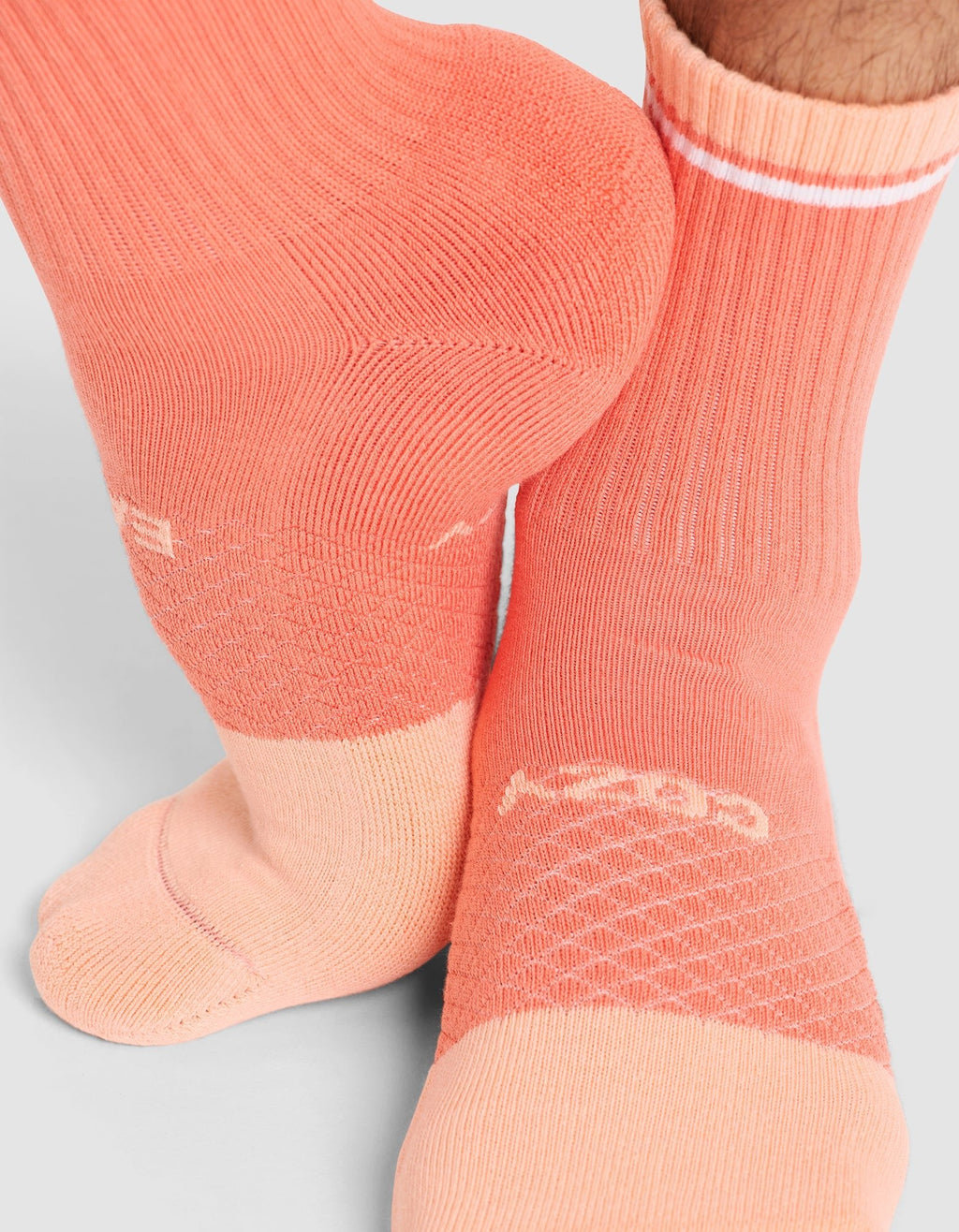 Close-up of a person wearing Cozy Earth Essential Calf Socks in peach and light pink with a textured pattern, white logo, and a white stripe near the top, standing on a light gray surface. |Color:Cantaloupe