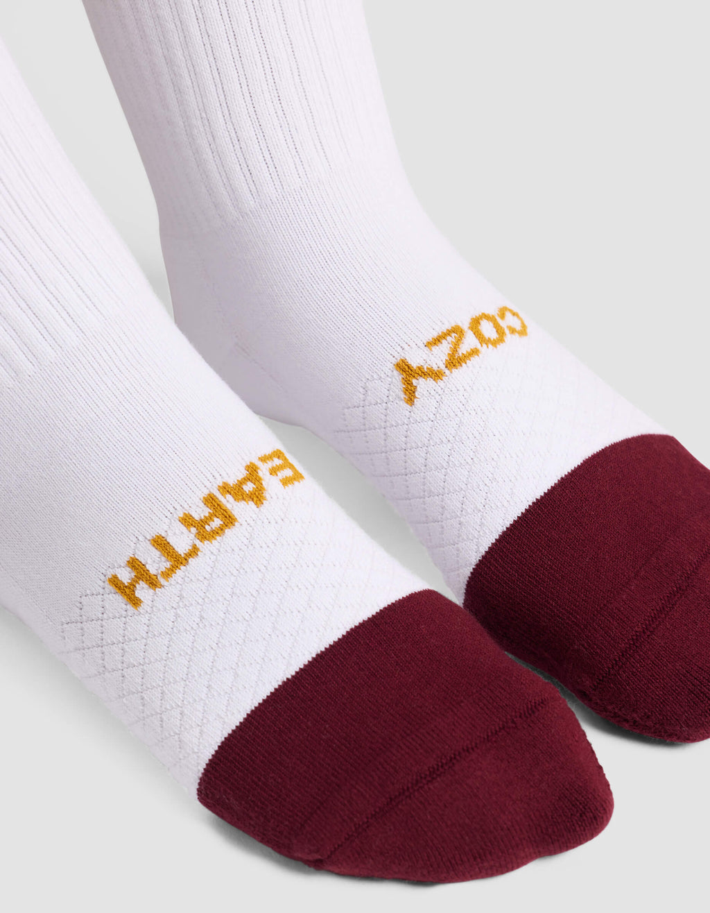 The Women's Essential Calf Sock by Cozy Earth features white fabric, maroon toes, "COZY EARTH" in gold on top, a ribbed upper section, and a textured midfoot pattern.|Color:Burgundy