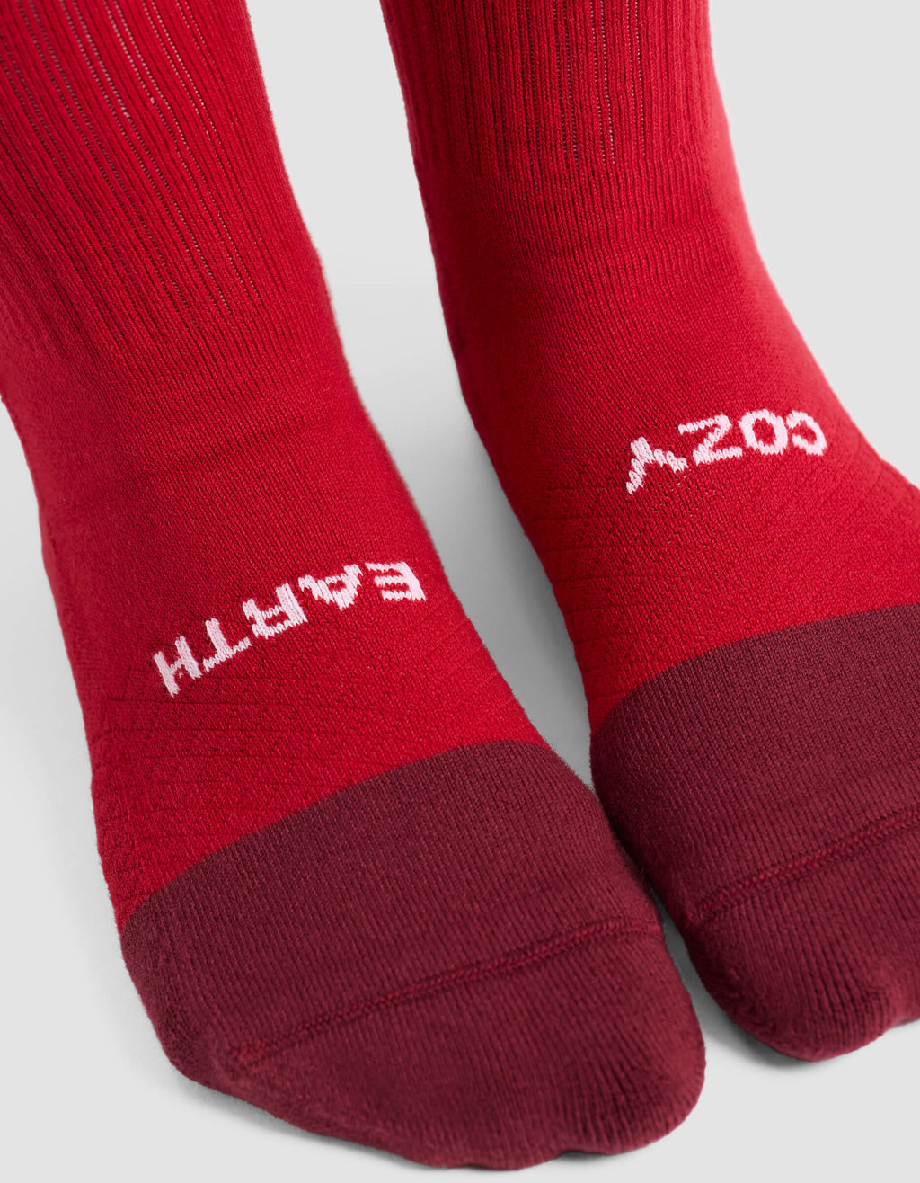 Close-up of feet wearing Cozy Earth Women's Essential Calf Socks in red with darker red toes. "EARTH" is printed on the left sock and "COZY" on the right, both in white text near the toes.|Color:Crimson