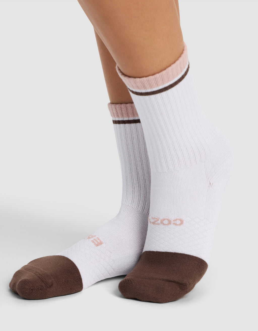 A person wearing Cozy Earth Essential Calf Socks—white with brown toes and heels, light pink cuffs, and a thin brown stripe near the top—stands on a light surface.|Color:Cedar
