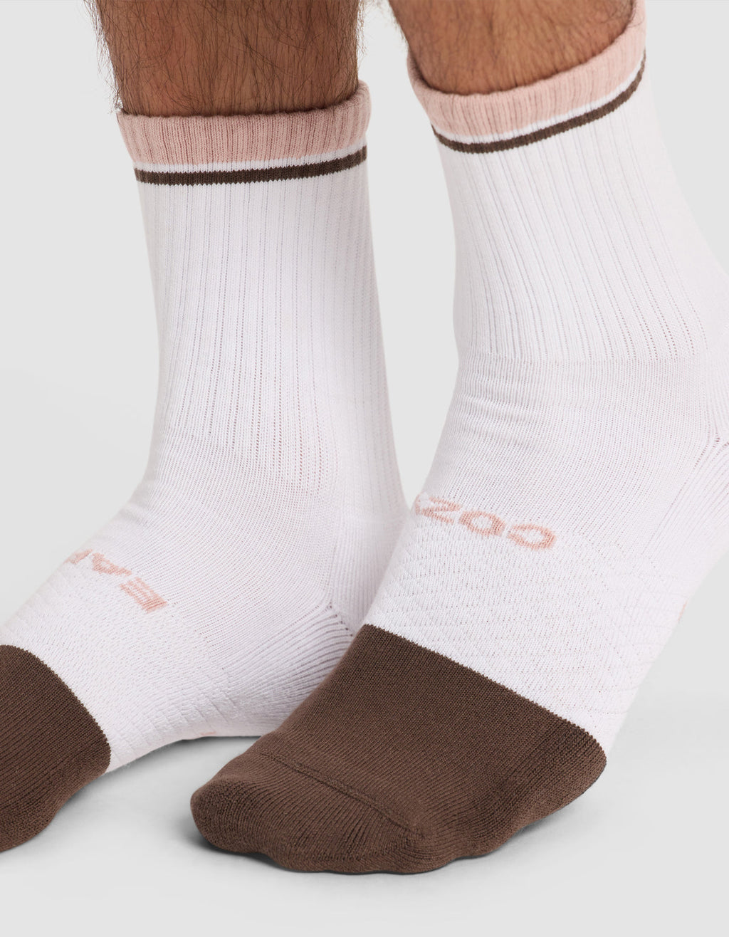 Two feet wear Cozy Earth Essential Calf Socks—white ribbed socks with brown toes and soles, pink accents at the top, a thin brown ankle stripe, and subtle pink text.|Color:Cedar