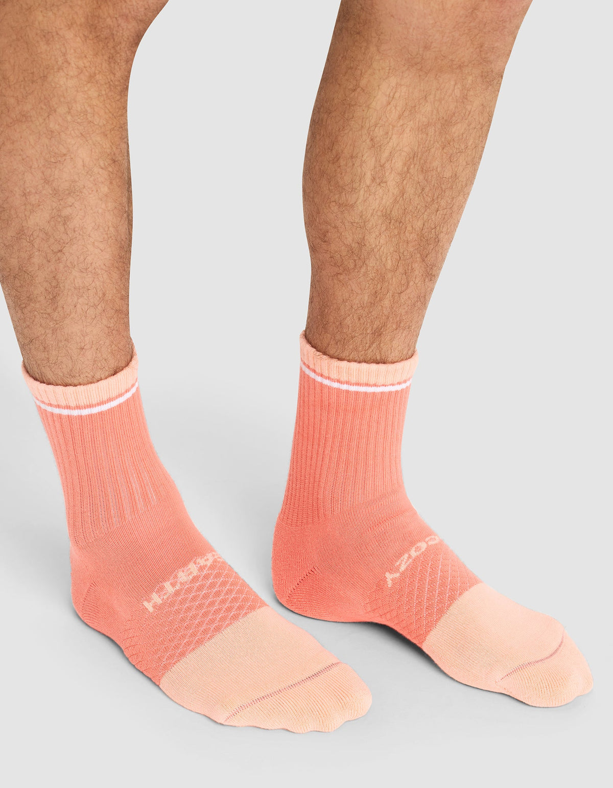 A person wears Cozy Earth Essential Calf Socks in peach with white text and accents, featuring ribbed cuffs and textured panels, standing on a light gray background. Only their lower legs and feet are visible.  |Color:Cantaloupe