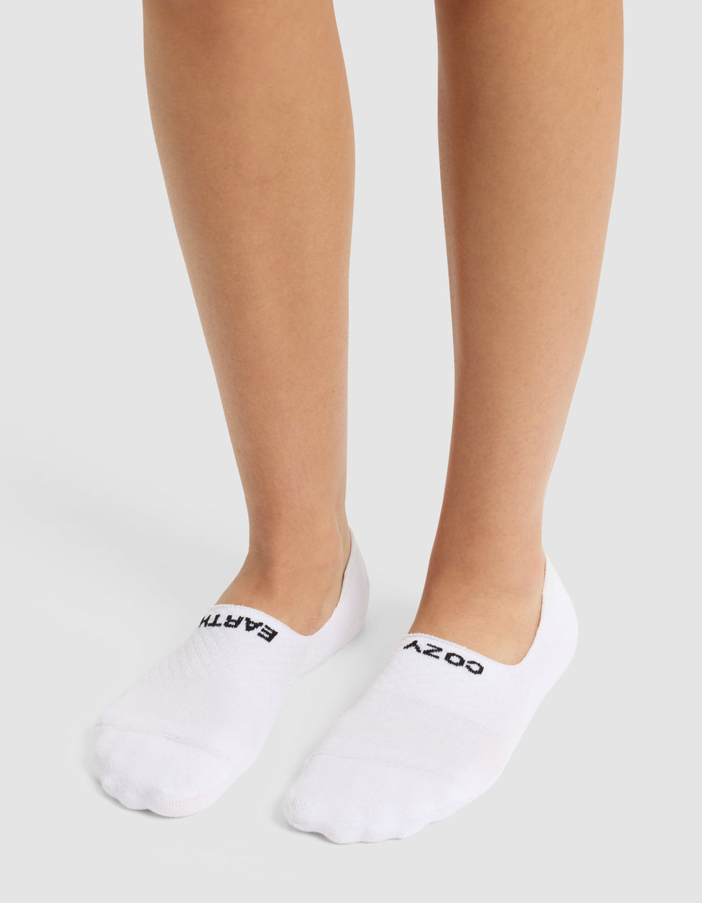 A person wears Cozy Earth's Essential No-Show Sock, featuring "COZY" and "EARTH" printed in black, while standing on a light surface.|Color:Burgundy