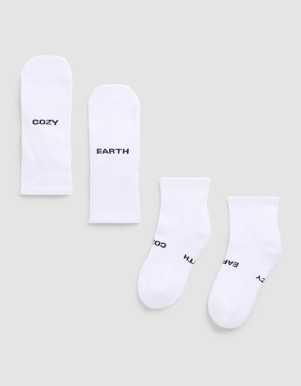 Four white Essential Quarter Socks from Cozy Earth are laid flat on a light gray background. Each features black text: one pair reads “COZY” and “EARTH,” while the other’s text shows parts of “EARTH,” “COZY,”.  |Color:White