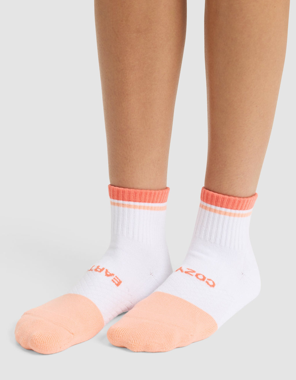 A person wears Cozy Earth Essential Quarter Socks in white with peach toes, heels, and cuffs. The socks feature text on the tops of the feet and are shown against a plain light gray background. |Color:Cantaloupe