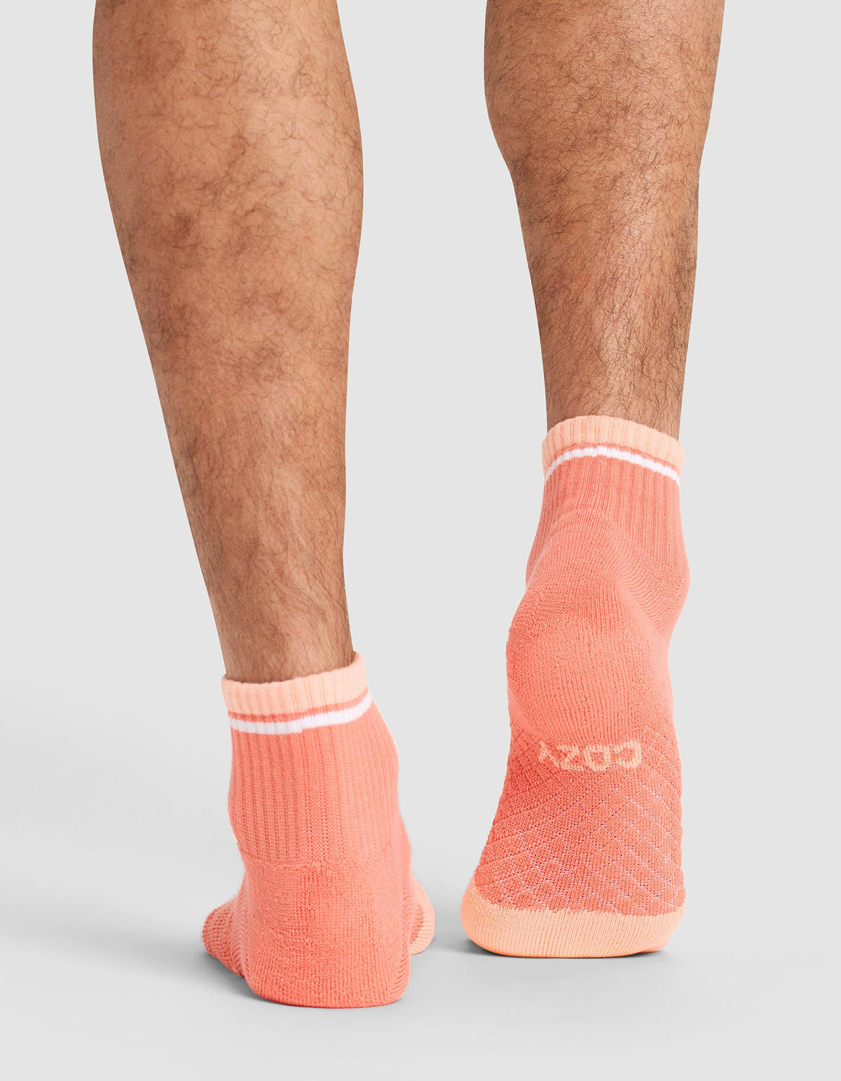 Back view of a person’s lower legs wearing Cozy Earth Essential Quarter Socks in coral with white cuffs and a white logo on the heel, set against a light gray background. |Color:Cantaloupe