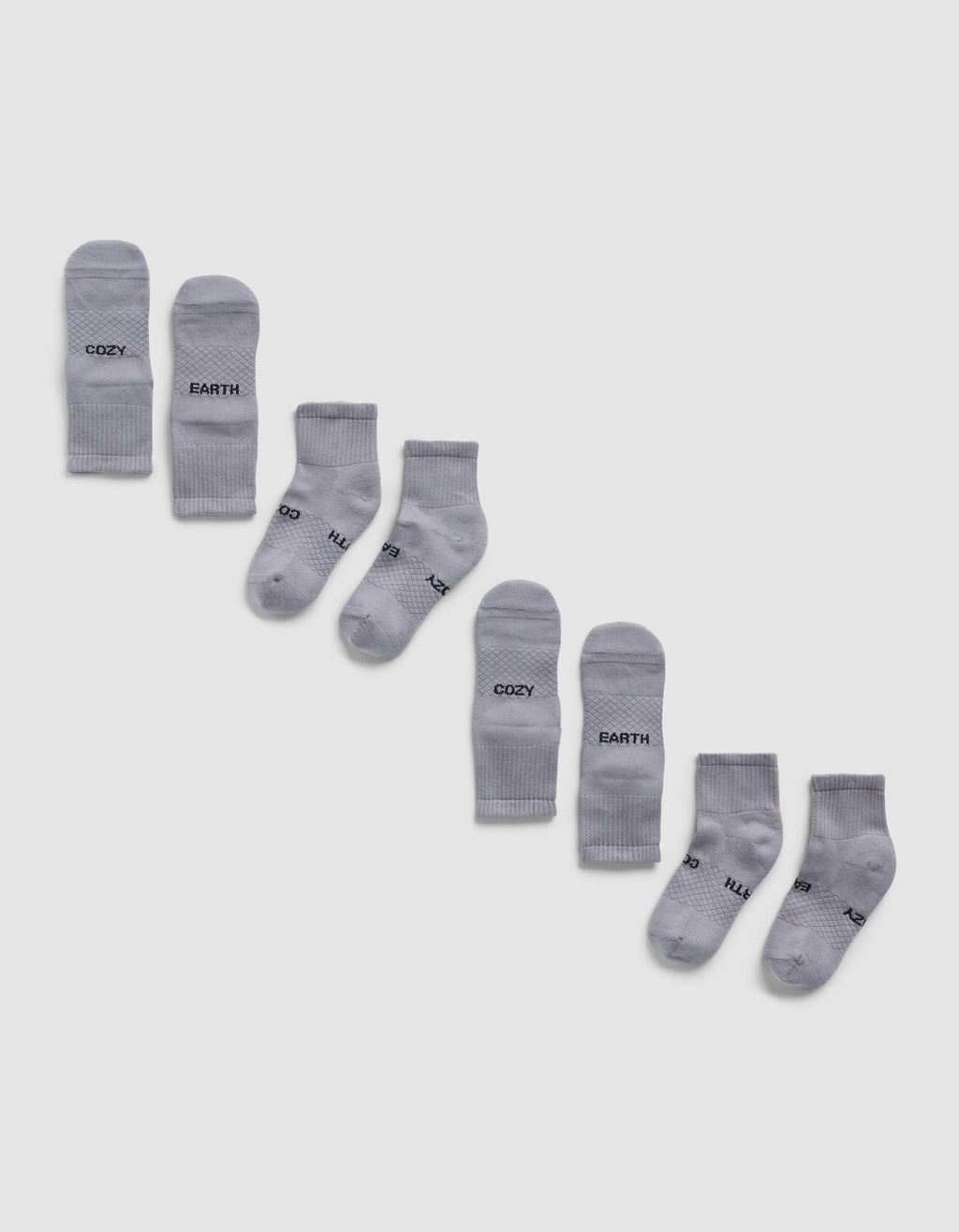 Four pairs of light gray Essential Quarter Socks by Cozy Earth are arranged diagonally on a white background, each pair featuring different words like "COZY," "EARTH," printed in black near the toes.|Color:Stone