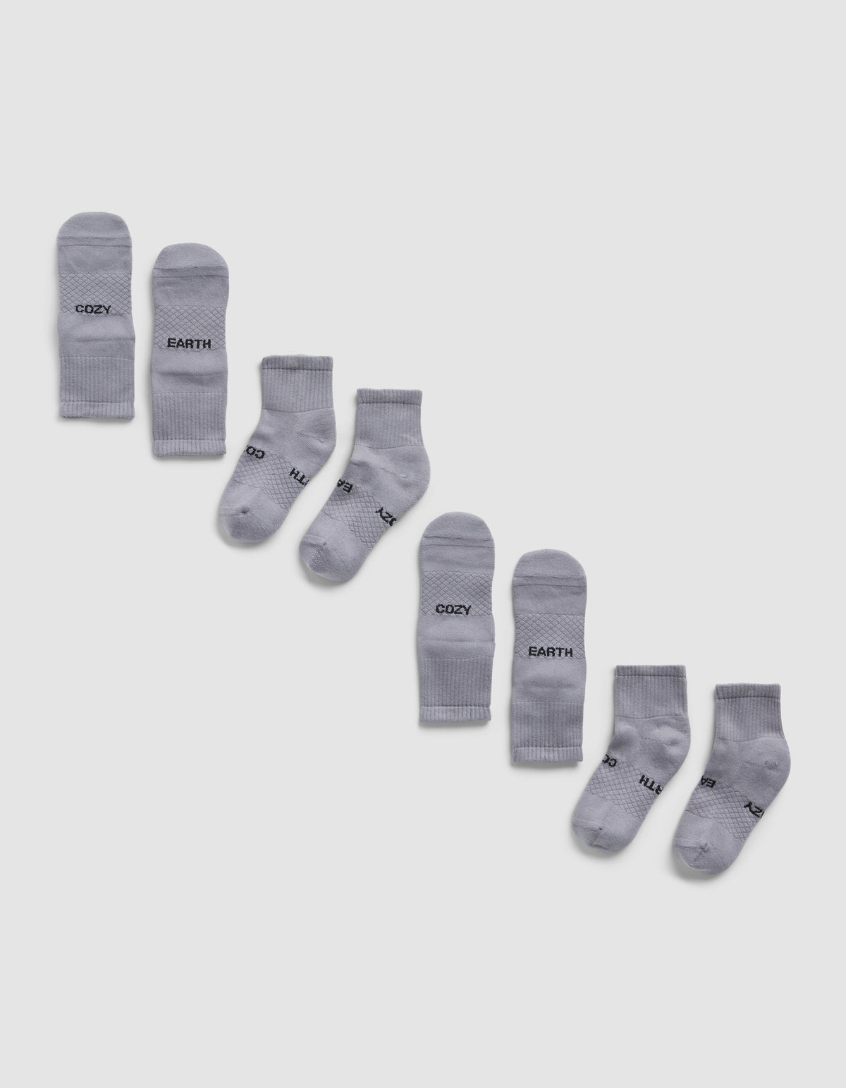 Four pairs of light gray Essential Quarter Socks by Cozy Earth are arranged diagonally on a white background, each pair featuring different words like "COZY," "EARTH," printed in black near the toes.|Color:Stone