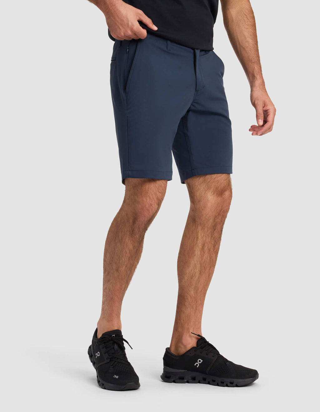 A person wearing a black t-shirt, Cozy Earth Men's Everywhere Short in navy, and black athletic shoes stands against a light gray background with one hand in their pocket.|Color:Eclipse