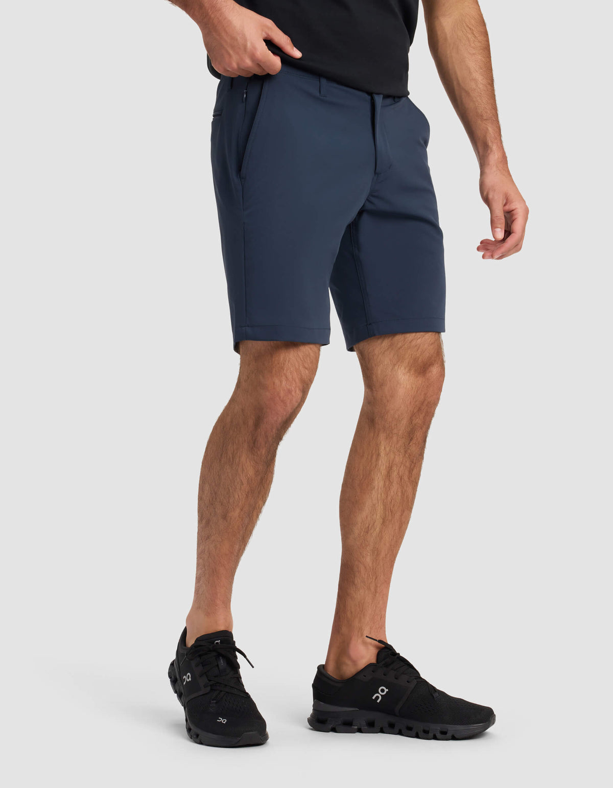 A person wearing a black t-shirt, Cozy Earth Men's Everywhere Short in navy, and black athletic shoes stands against a light gray background with one hand in their pocket.|Color:Eclipse