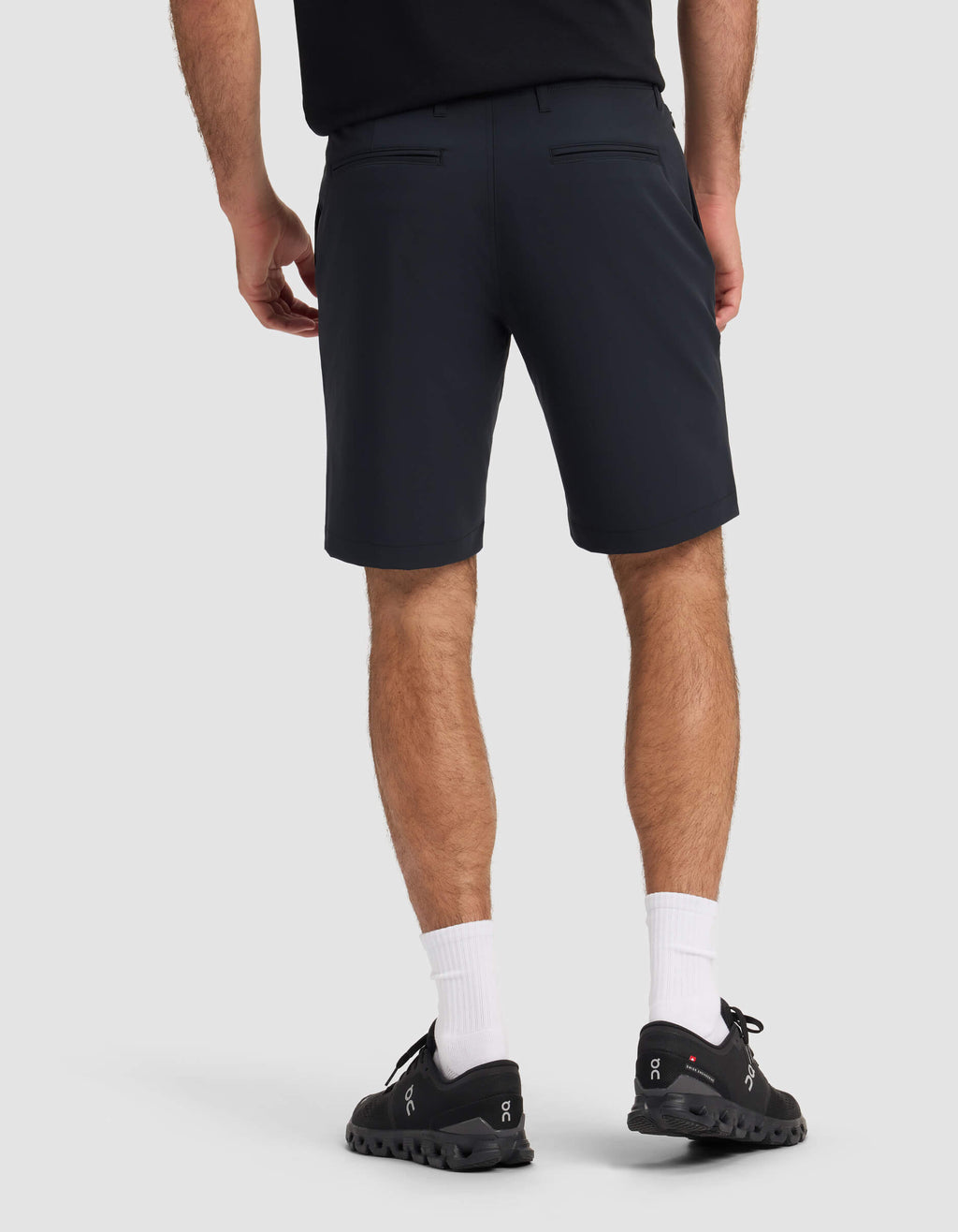 A person is standing facing away, wearing a black shirt, Cozy Earth Men's Everywhere Short in dark navy, white crew socks, and black athletic shoes against a plain light background.|Color:Jet Black