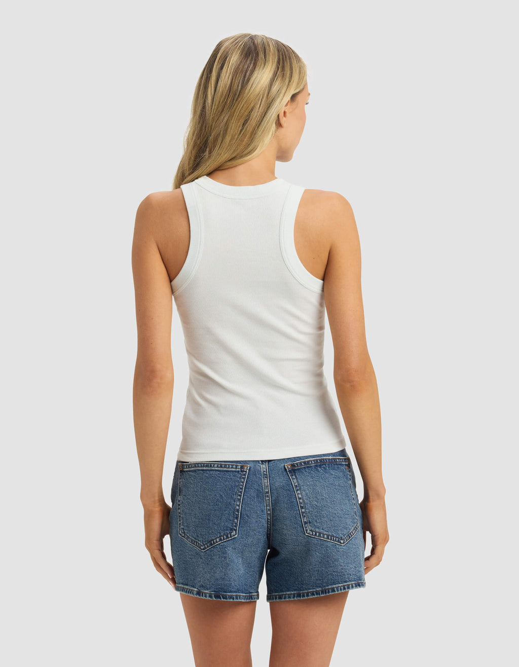A woman with long blonde hair is seen from the back wearing the Cozy Earth Women's Fine Ribbed Tank in white and blue denim shorts, set against a light gray background.|Color:Vapor