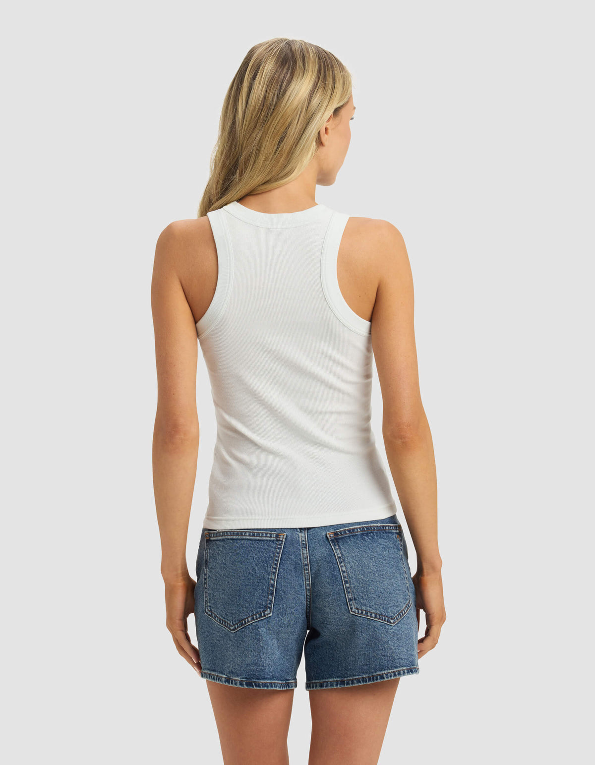 A woman with long blonde hair is seen from the back wearing the Cozy Earth Women's Fine Ribbed Tank in white and blue denim shorts, set against a light gray background.|Color:Vapor