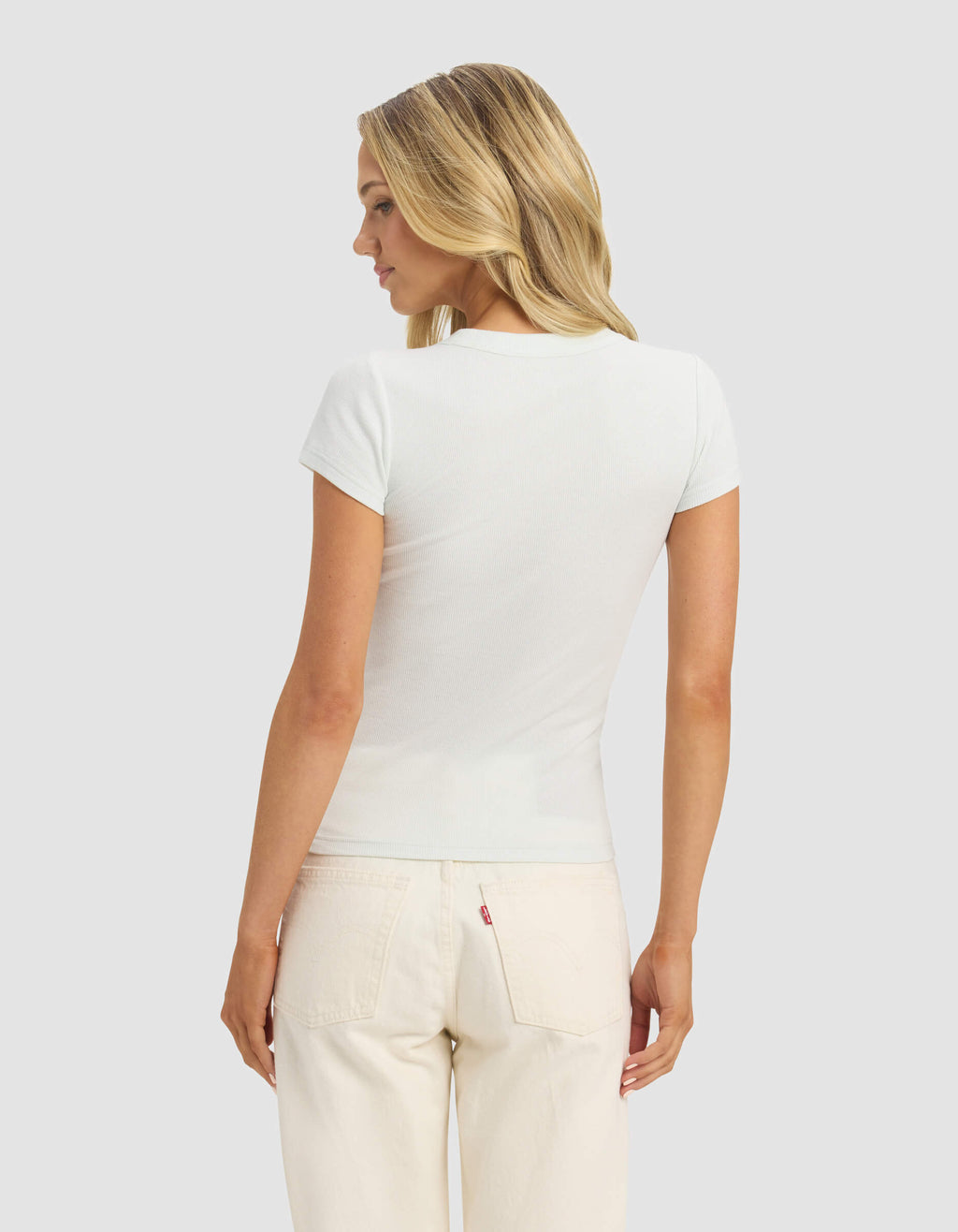 A woman with blonde hair faces away, wearing the Cozy Earth Women's Fine Ribbed Tee in white and light-colored jeans, set against a plain light gray background.|Color:Vapor