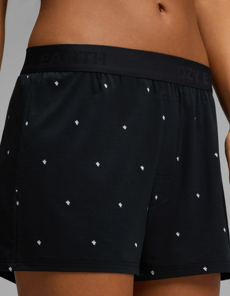 Close-up of a person wearing Cozy Earth Women’s First Layer Pajama Boxer Shorts in black with a small white dot pattern. The waistband is black with subtle text branding, and the background is plain gray.|Color:Mini Ghost