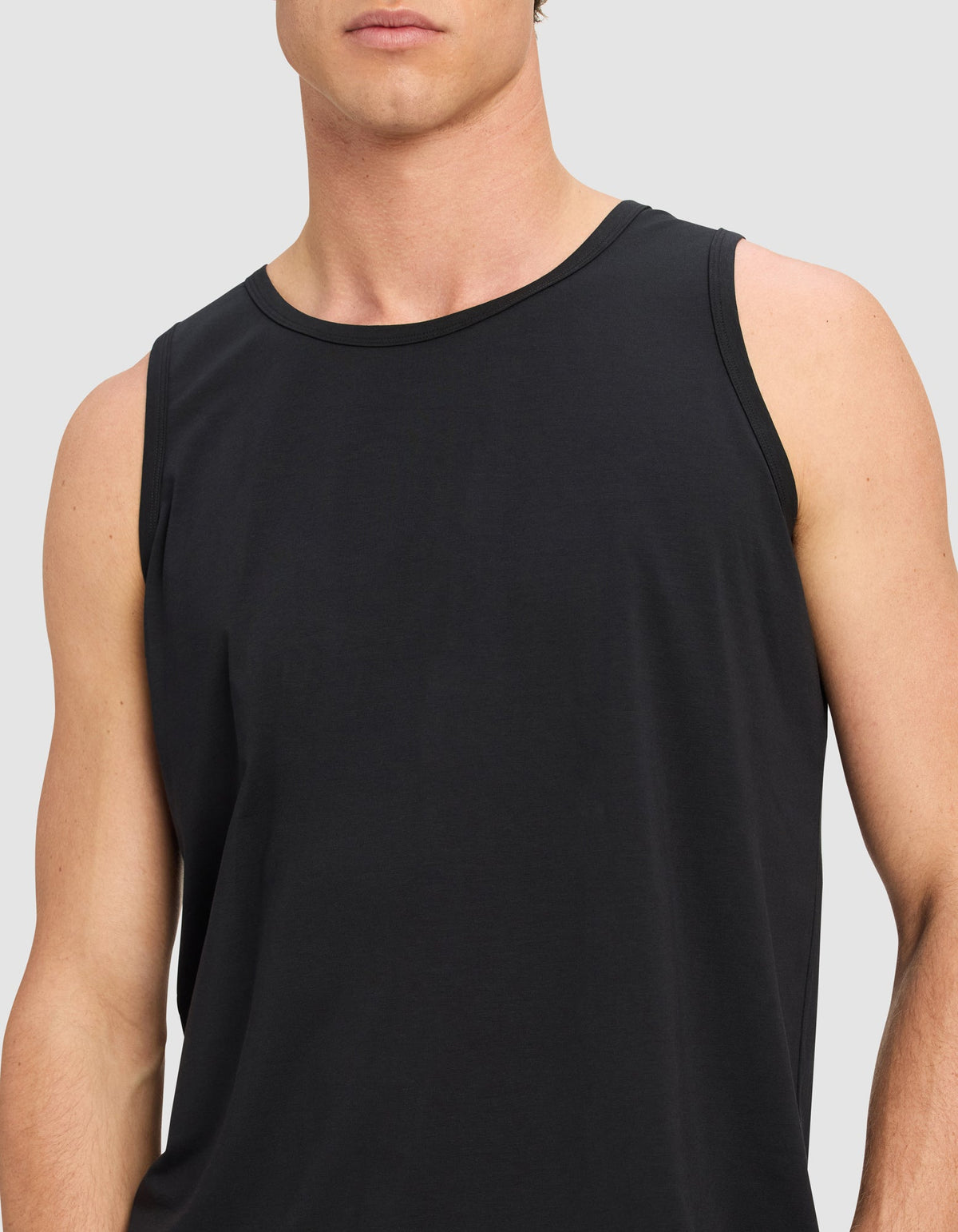 A model wears the Cozy Earth Men's First Layer Pajama Tank in black, shown from shoulders to waist against a plain light gray background. The person's face is partially out of frame.|Color:Jet Black