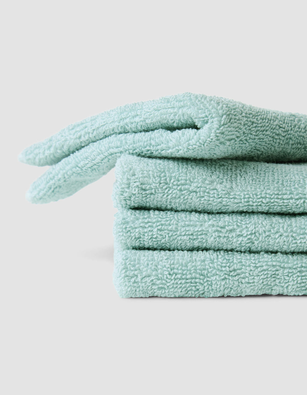 Three neatly folded Complete Cleansing Cloths by Cozy Earth, in light teal, are stacked on a plain light gray surface. The cloths have a soft, fluffy texture and appear clean and new.|Color:Tide