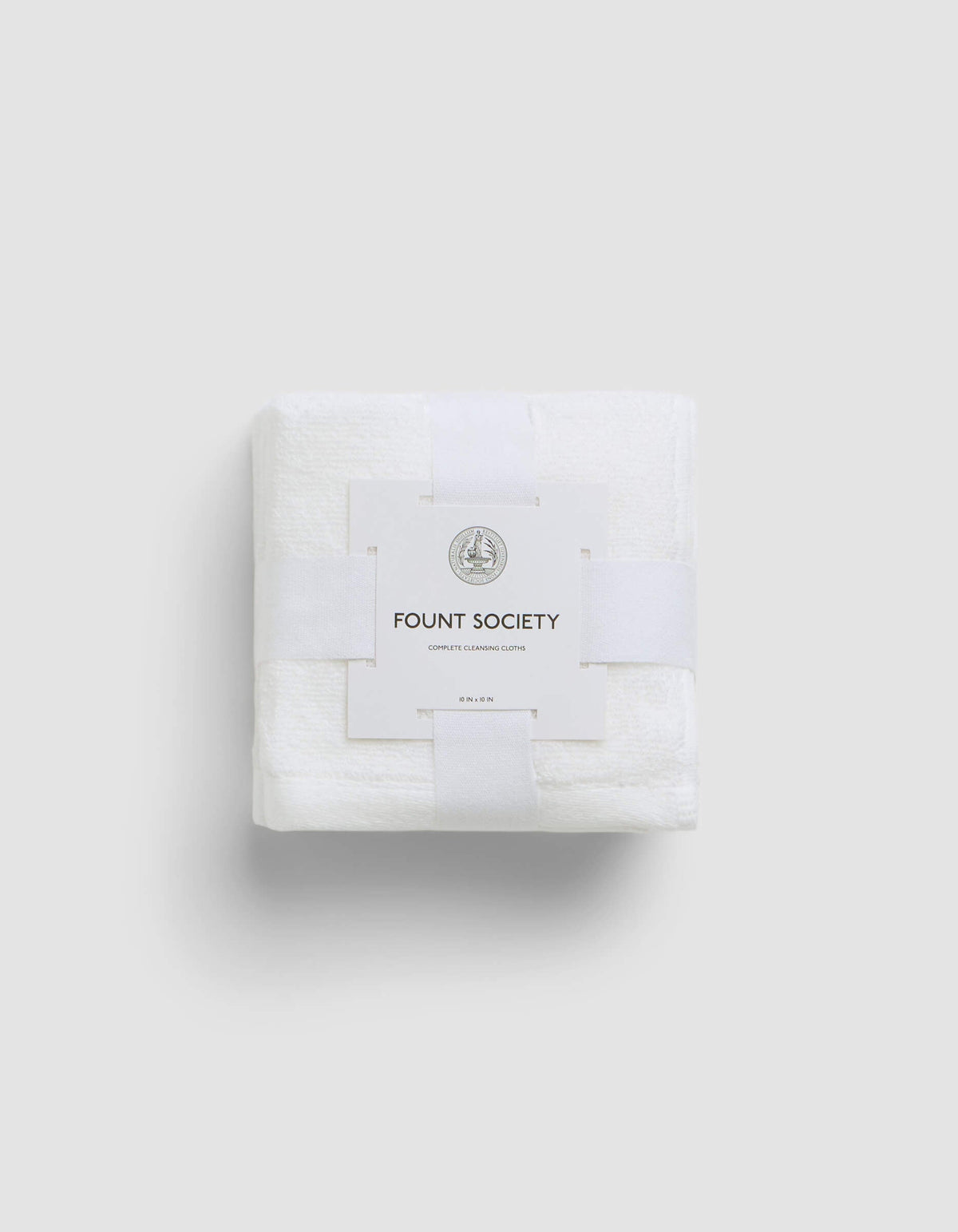 A neatly folded white Complete Cleansing Cloth by Cozy Earth, wrapped with a white paper band featuring the brand name and a small circular logo, set against a plain light gray background.|Color:White
