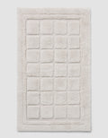 The Cozy Earth Grid Bath Mat is a rectangular, off-white mat with a raised grid design and a thick, fluffy border.|Color:Light Grey
