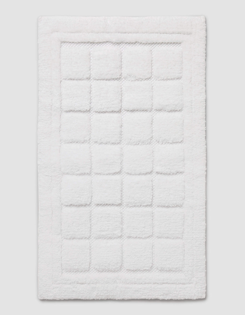 The Cozy Earth Grid Bath Mat is a white, rectangular mat featuring a textured square pattern in the center and a raised border around the edge, shown on a plain background.|Color:White