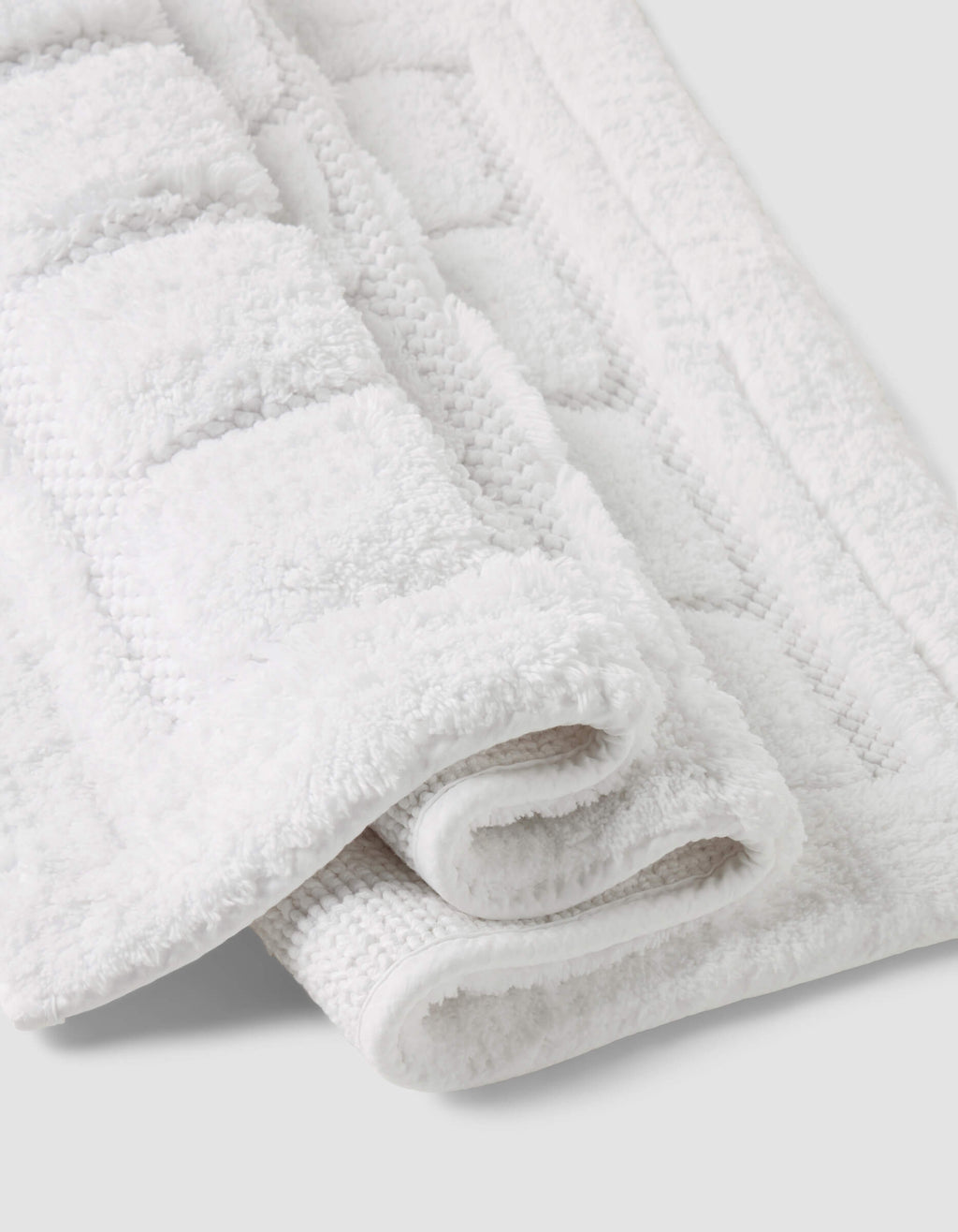 A close-up of the Folded Grid Bath Mat by Cozy Earth, featuring a white textured geometric pattern, displayed on a light gray background.|Color:White