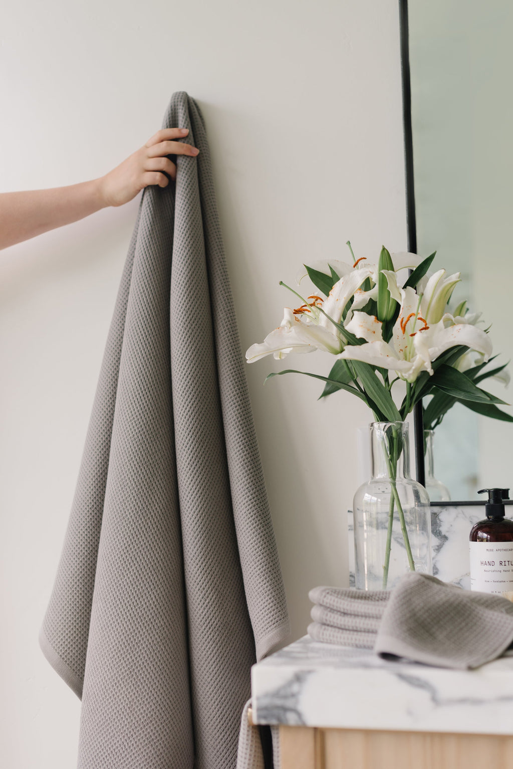 Waffle Bath Towel in the color Charcoal. Photo of Charcoal Waffle Bath Towel taken with Charcoal Waffle Bath Towel hanging from towel hook in a bathroom with white walls |Color:Charcoal