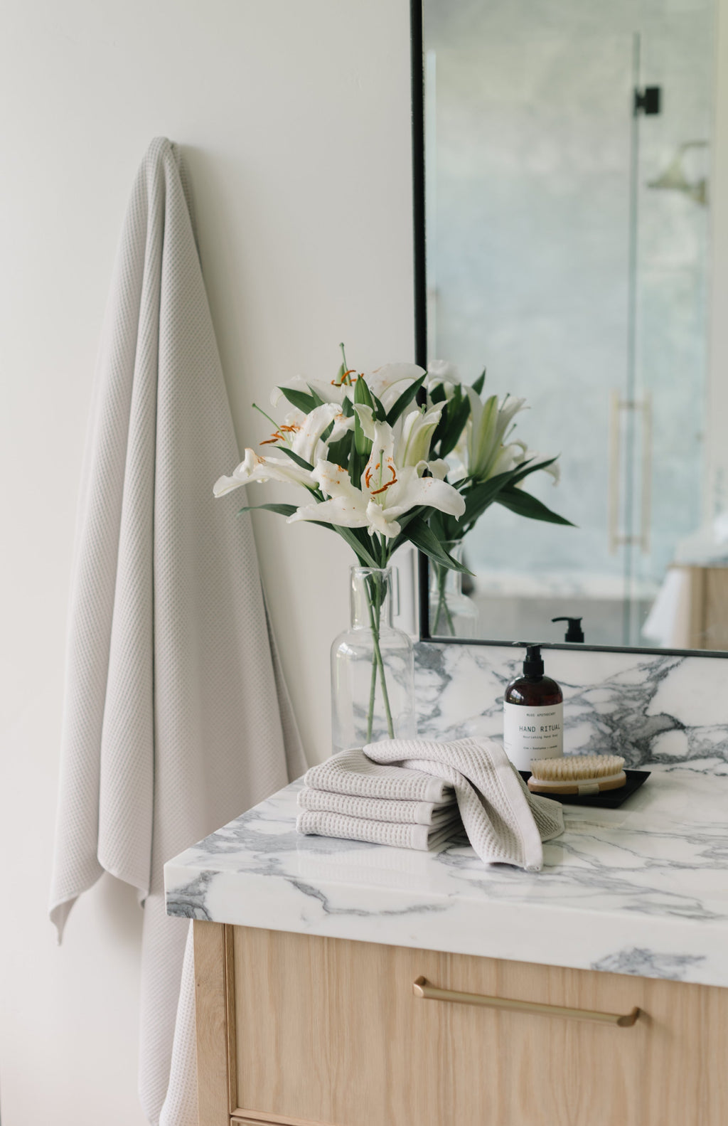 Light Grey Waffle Hand Towel hanging from a gold towel bar. The photo was taken at a white marble bathroom sink. A Waffle Bath Towel is seen hanging on the wall in the background. |Color:Light Grey