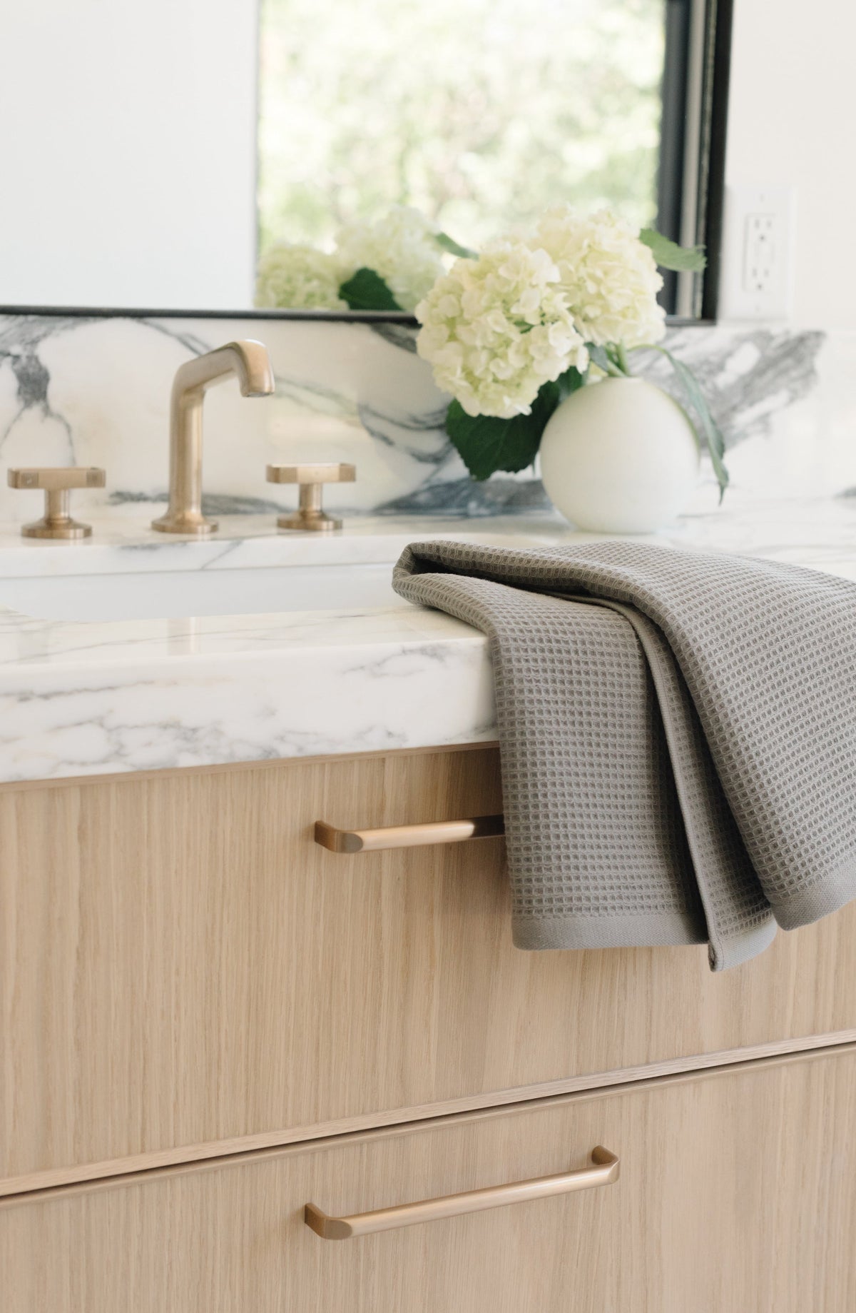 Charcoal Waffle Hand Towel resting folded on a white marble bathroom sink. The towel is folded so that different views of the towel can be seen. |Color:Charcoal