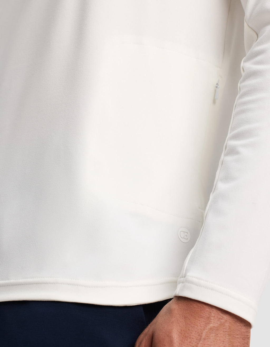 A close-up of a person wearing the Cozy Earth Men's Lightweight Performance Hoodie in white, highlighting the lower hem, a small logo detail, and part of the person's hand.|Color:White