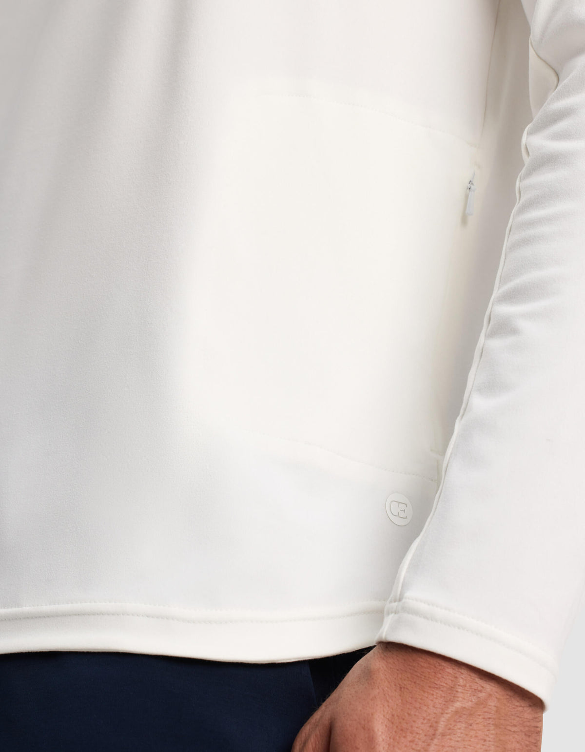 A close-up of a person wearing the Cozy Earth Men's Lightweight Performance Hoodie in white, highlighting the lower hem, a small logo detail, and part of the person's hand.|Color:White