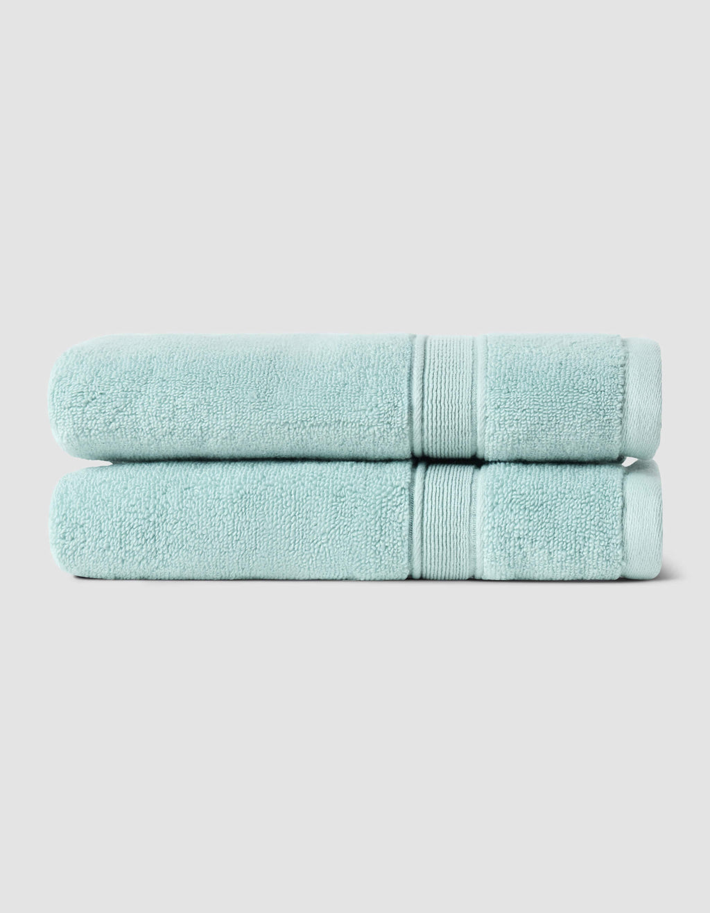 Two Luxe Bath Towels by Cozy Earth, neatly folded and stacked, are displayed against a plain light gray background.|Color:Tide