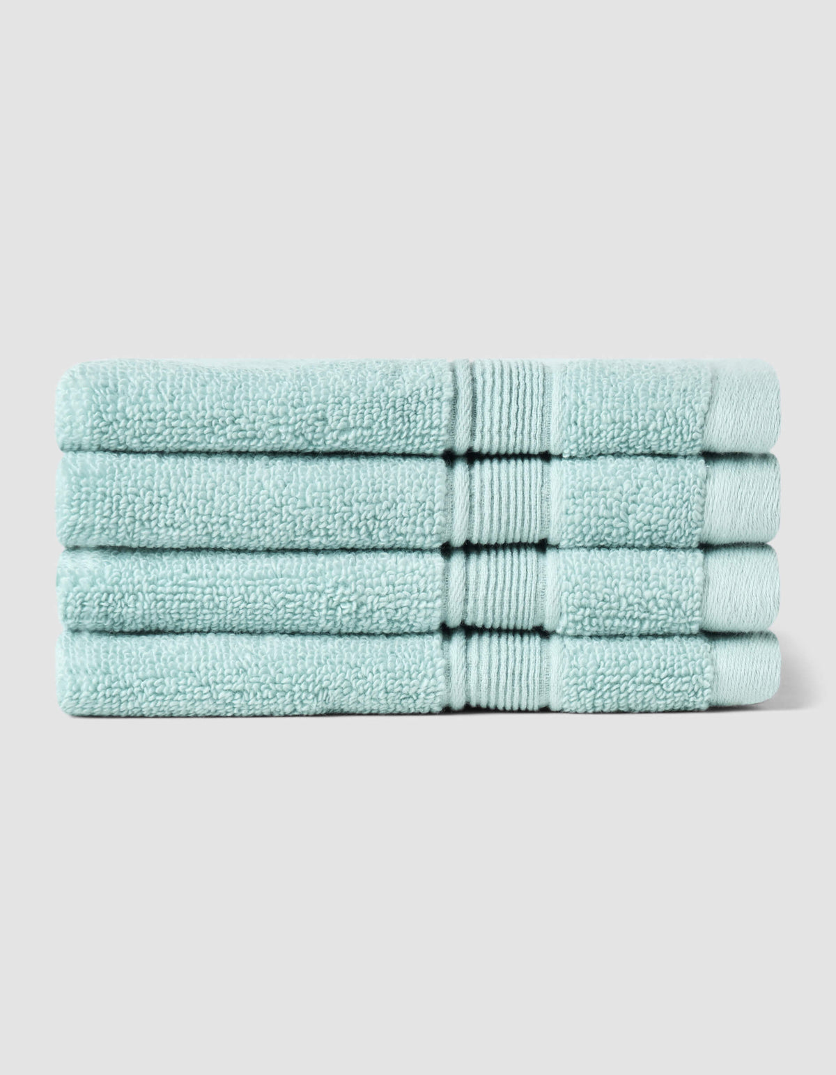 Four neatly folded Luxe Bath Towel Set towels by Cozy Earth are stacked atop one another against a plain, light gray background.|Color:Tide