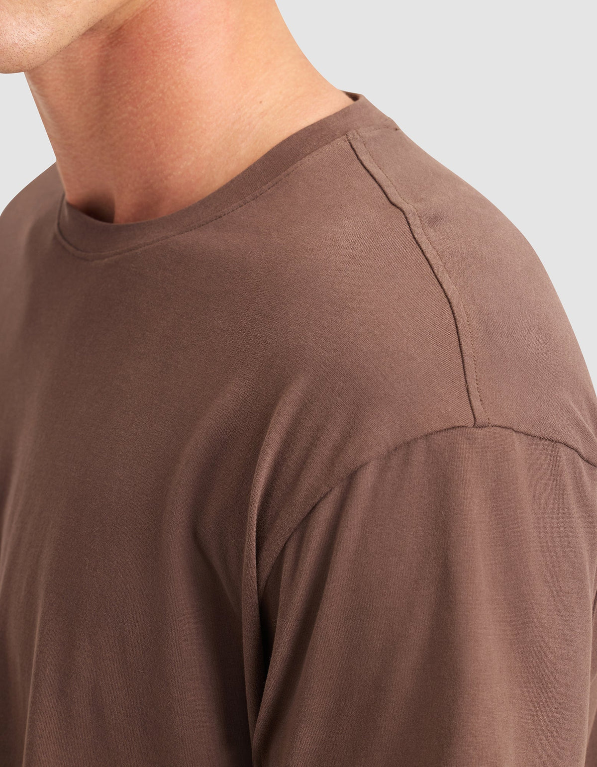 Close-up of a person wearing the Cozy Earth Men's All Day Tee in brown, highlighting the crew neckline, shoulder, and upper chest against a light gray background. |Color:Cacao