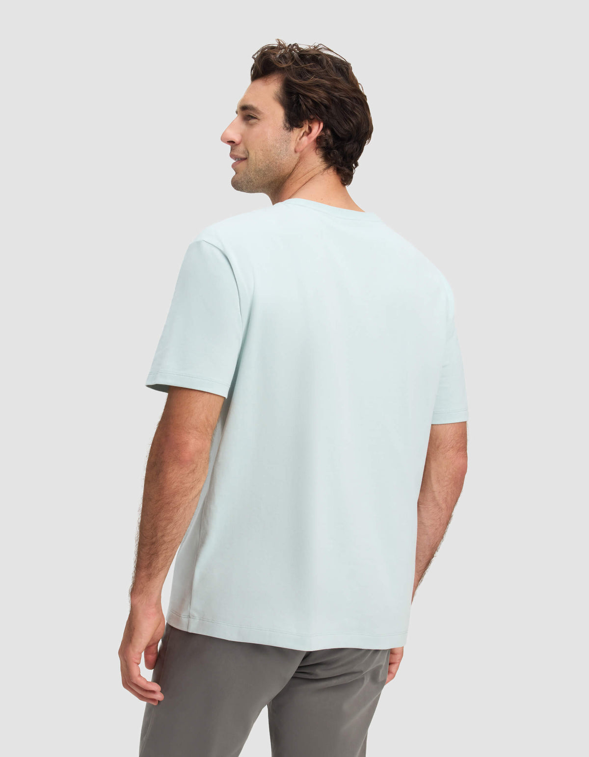 A man with short brown hair faces away, wearing the Cozy Earth Men's All Day Tee in light blue and gray pants, set against a plain light gray background.|Color:Tide