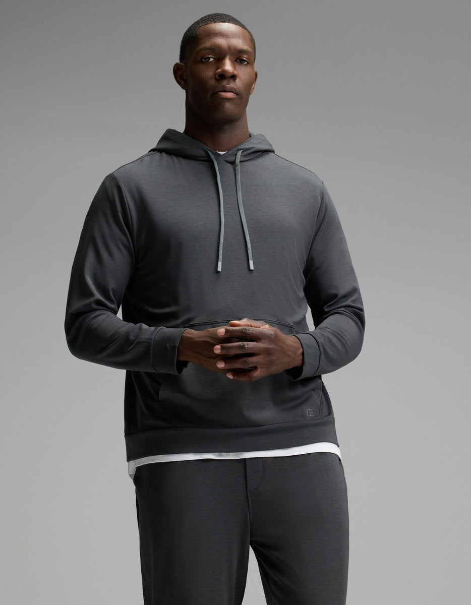 A man stands against a plain gray background wearing the Cozy Earth Men’s Brushed Bamboo Hoodie & Jogger Set, with his hands clasped together in front of him.|Color:Charcoal