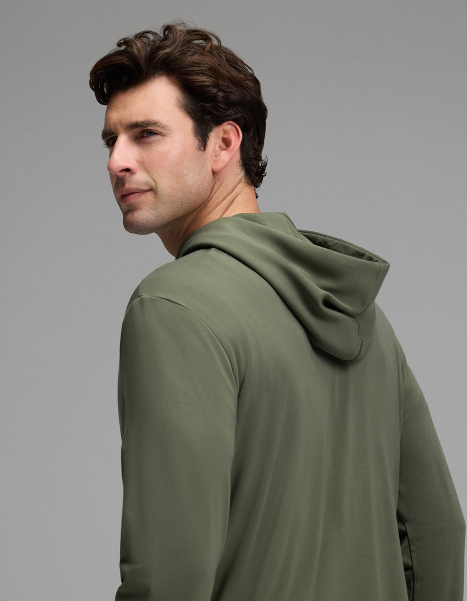 A man with short brown hair models the Cozy Earth Men’s Brushed Bamboo Hoodie in olive green, glancing over his shoulder against a plain gray background.|Color:Olive