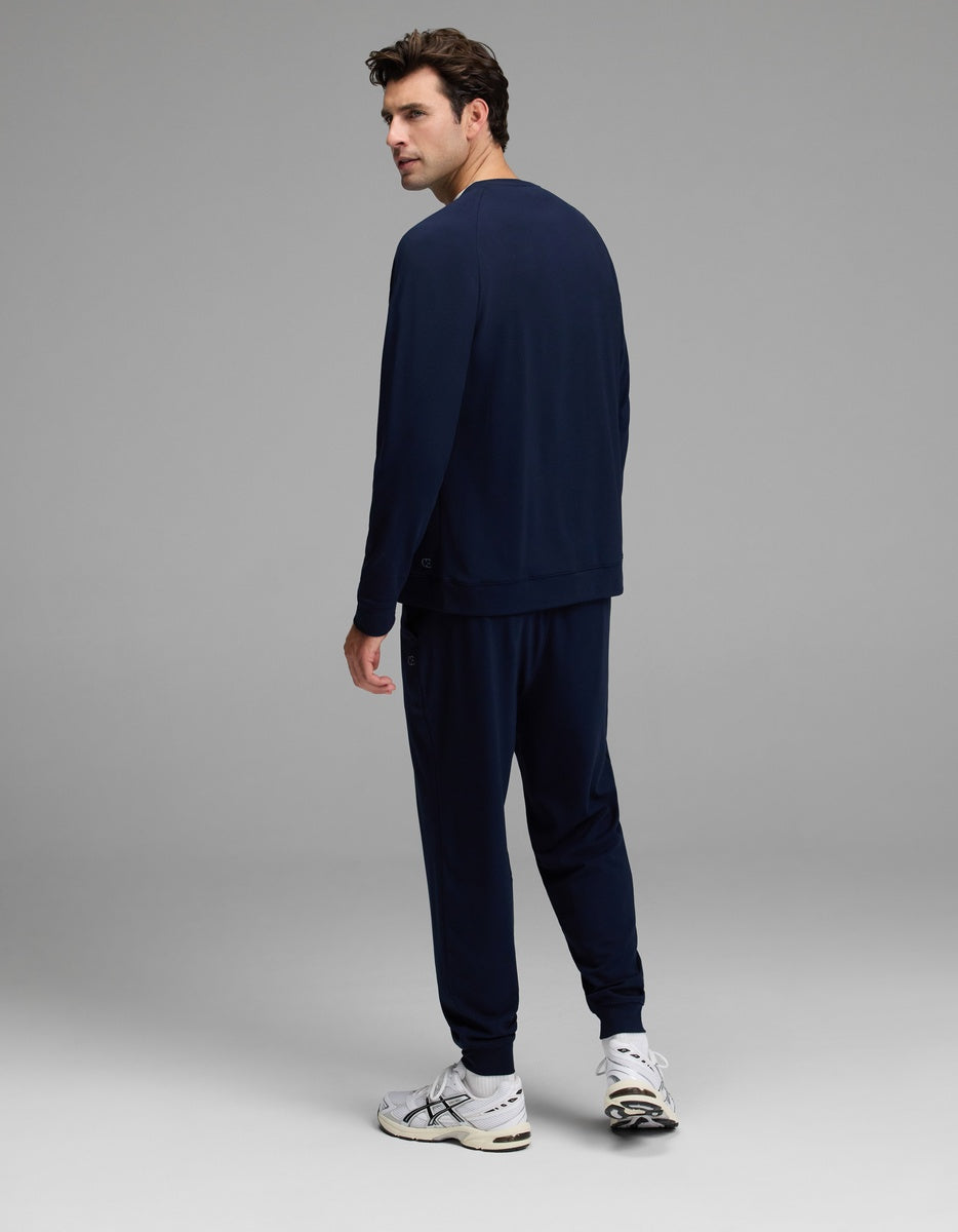 A man dressed in the Cozy Earth Men’s Brushed Bamboo Jogger Set and white sneakers stands facing slightly away, looking back over his shoulder against a plain gray background.|Color:Navy