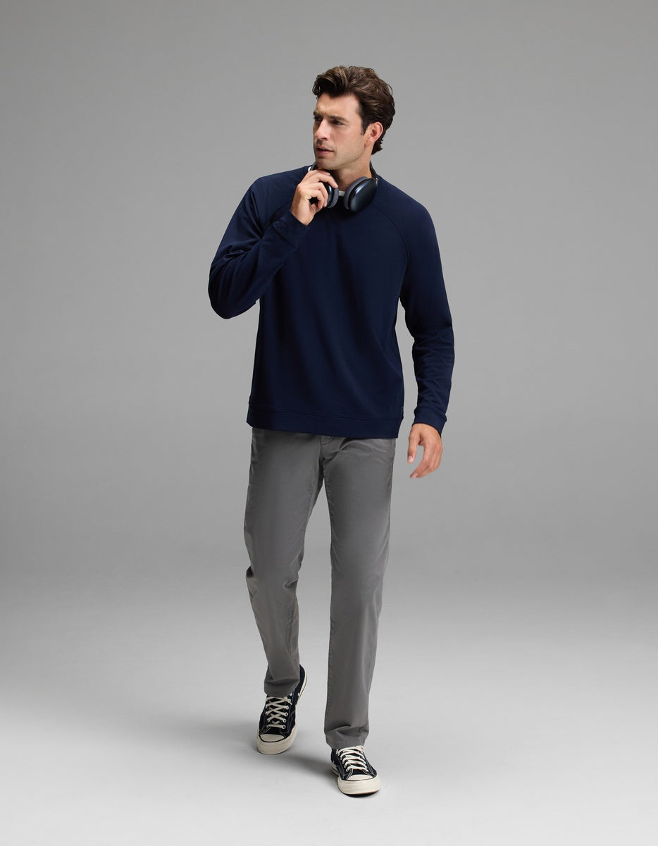 A man wearing the Cozy Earth Men’s Brushed Bamboo Pullover Crew in navy, paired with gray pants and black sneakers, walks forward holding black headphones near his chin against a plain light gray background.|Color:Navy