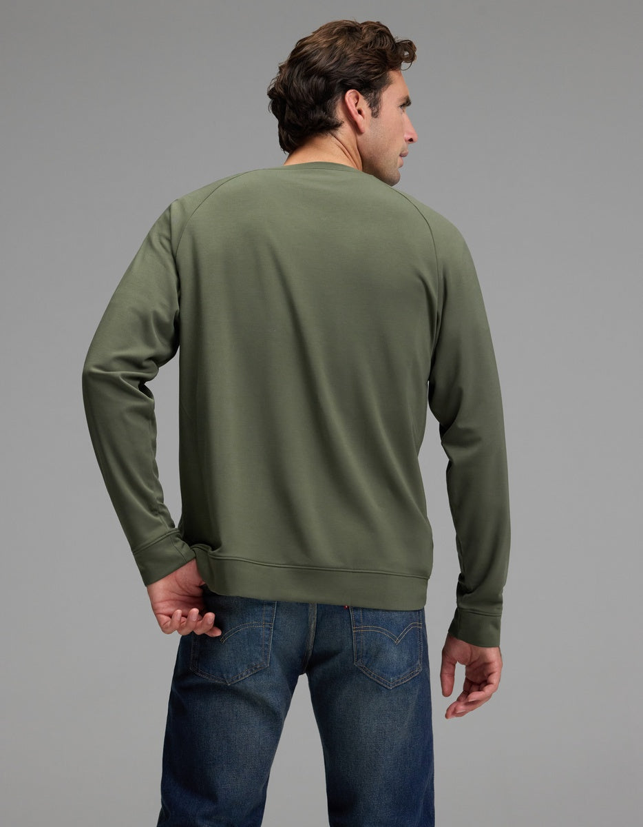 A man is seen from behind, his head turned slightly to the left, wearing the Cozy Earth Men’s Brushed Bamboo Pullover Crew in olive green and blue jeans, set against a plain gray background.|Color:Olive
