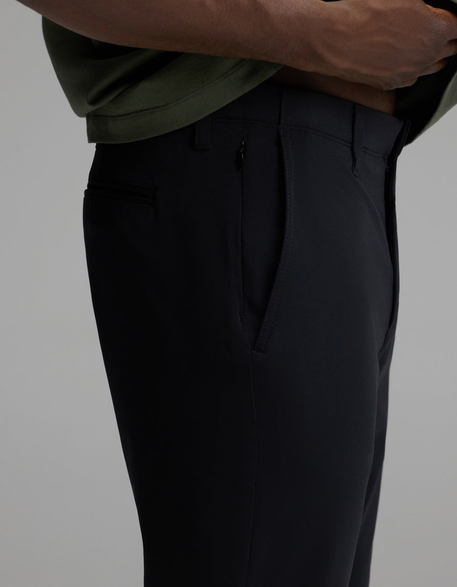A person wearing Cozy Earth’s Men’s Everywhere Pant in black and a green shirt stands with one hand near the waistband, highlighting a close-up side view of the pant’s pocket and tailored fit.|Color:Jet Black