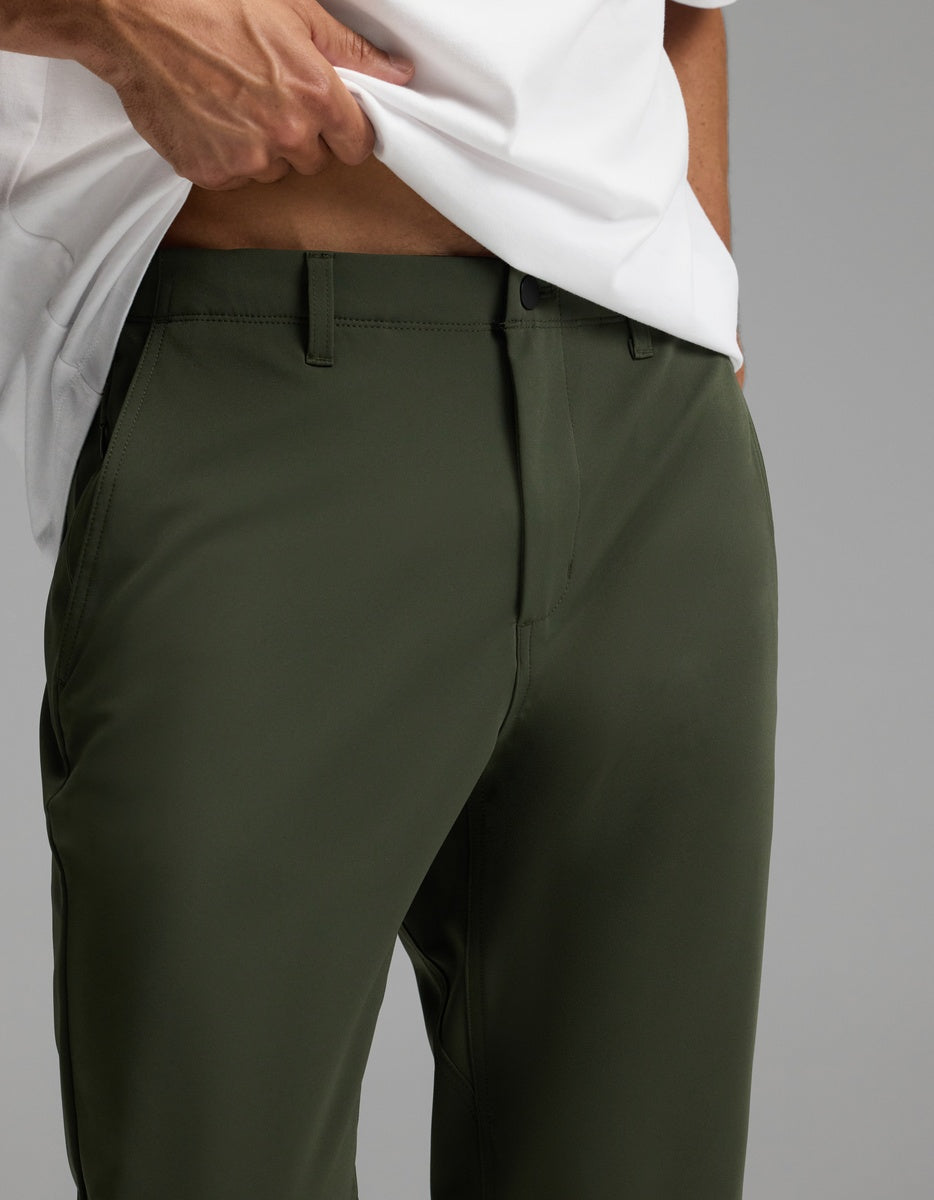 A person models the Cozy Earth Men’s Everywhere Pant in olive green, paired with a white shirt. They stand against a plain gray background, lifting the shirt slightly to reveal part of their midriff.|Color:Olive