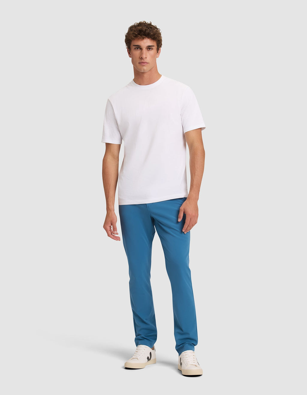 A man stands against a light gray background, wearing Cozy Earth's Men's Everywhere Pant in blue, a plain white short-sleeve t-shirt, and white sneakers. He faces forward with a neutral expression and relaxed posture.  |Color:Wave