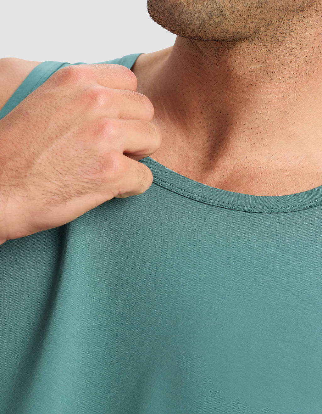 A close-up shows a person wearing the Cozy Earth Men's First Layer Pajama Tank in teal, holding the fabric near their shoulder with their right hand, with only the lower half of their face visible.|Color:Sea Green