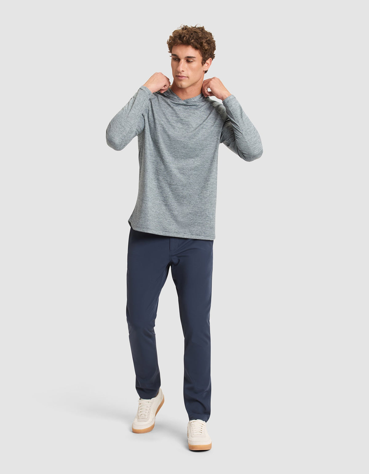 A man stands against a plain background, wearing the Cozy Earth Men's Lightweight Performance Hoodie. He looks to the side, holding the hoodie’s collar with both hands. |Color:Heather Dawn