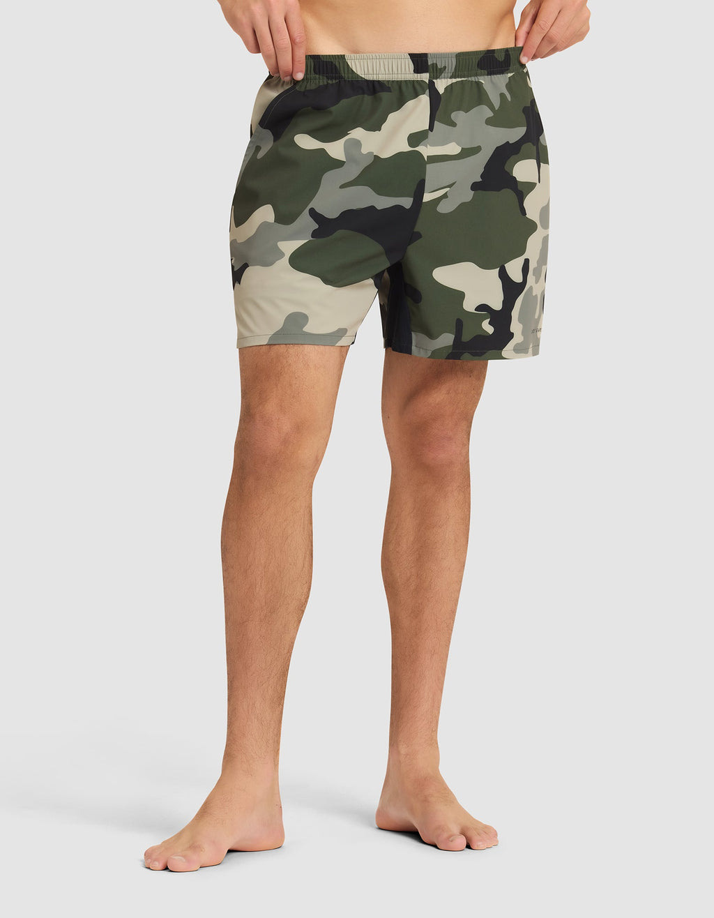 A person stands barefoot in Cozy Earth Men's Day & Night Shorts 5" against a plain light background, showing only the lower torso and legs. |Color:Cypress Camo